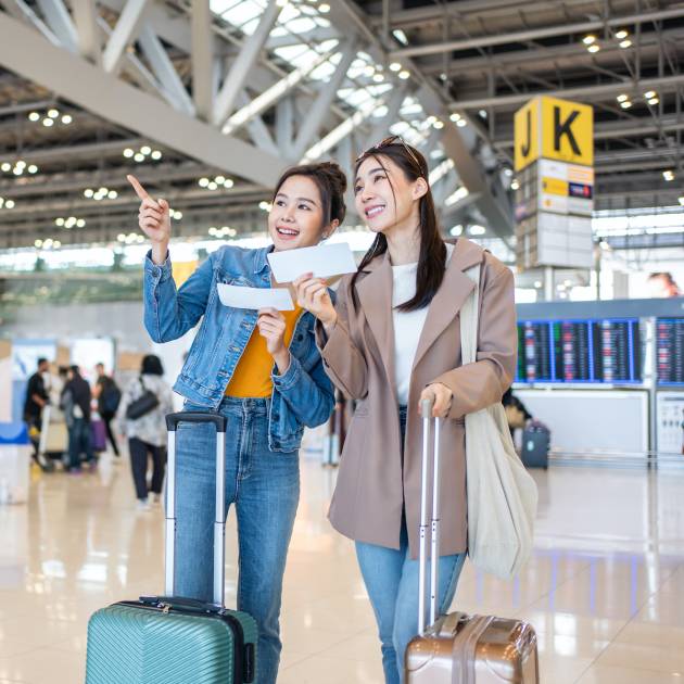 Asian young women passenger walk in airport terminal to boarding gate. Attractive beautiful female tourist friends feeling happy and excited to go travel abroad by airplane for holiday vacation trip.
