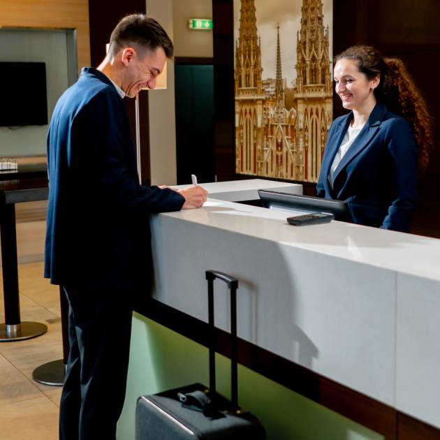 The receptionist at the counter meets the guest with luggage in hotel business travel hospitality