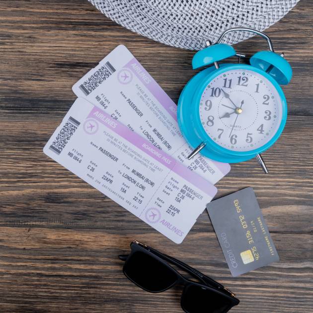 top view of blue alarm clock with airplane tickets credit card and sunglasses on a wooden background with copy space
