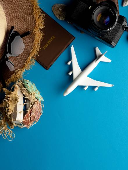 Airplane model, sunglasses, passport and camera on blue background with copy space. Travel, transport and vacation.